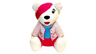 Bear with a bright red bandana, jacket, trousers and lipstick. Also with bright blue top and gold hoop earrings.