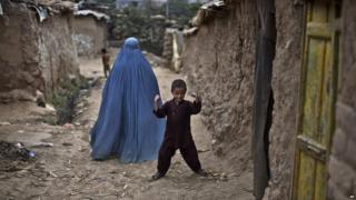 A young boy and a woman in a burka behind him in an alley