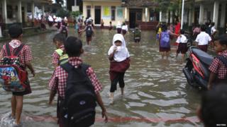 A student drinks a packet of milk as she wades through flood waters in Lopang Domba Elementary School