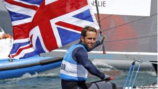 Ben Ainslee holding the British flag on a sailing boat