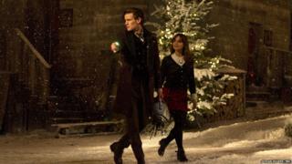 Matt Smith as the Doctor with Jenna Coleman as Clara. The Doctor is carrying a Cyberman's head.