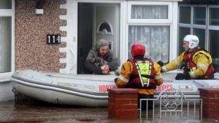 A woman and her dog are rescued by the RNLI or Royal National Lifeboat Institute, from floods as heavy seas and high tides sweep across the country, in Rhyl, Wales