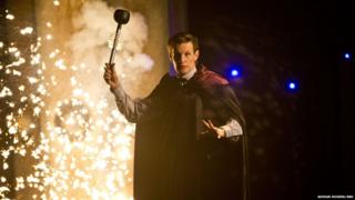 Matt Smith wields a Dalek's eye stalk as an explosion goes off behind him.