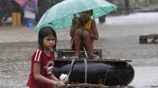 A girl pulls her brother on a makeshift raft along a flooded portion of a road in Butuan City.