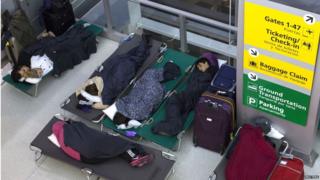 Family sleeping on camping beds in an airport lounge
