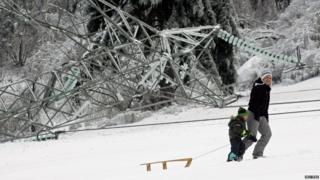 A woman and child walk past a fallen pylon with a sledge.