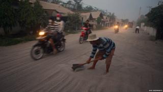 Man clears a road covered in ash