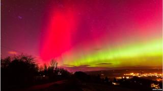 The Aurora Borealis seen in pink and orange over a British landscape