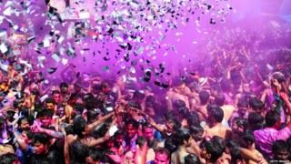A crowd of people are covered in confetti and purple paint