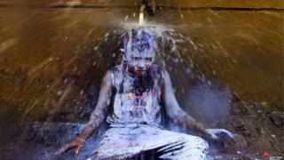 A boy sits under a tap to wash off paint
