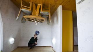 Woman poses in upside-down house.