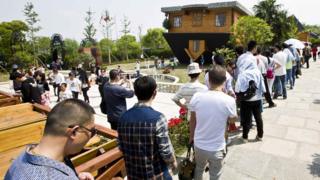 Queue of people at upside-down house.
