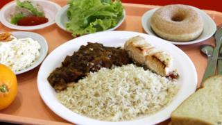 A school lunch consisting of rice, salmon, ratatouille, a slice of bread, a salad with celery and carrots, and an orange and donut is laid out on a tray at the Anne Franck school in Lambersart, northern France
