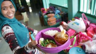 Sri, a house maid, shows a lunch box she prepared for her employer's child, at an elementary school in Jakarta, Indonesia. The lunch consists of rice, meatball soup, and tofu and vegetables.