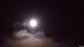The moon is hanging just above a group of clouds that are being lit up by the moon.