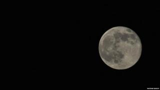 The large white moon sits on the right-hand side of a dark black sky.