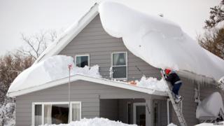 Man climbing on to roof of snow-covered home