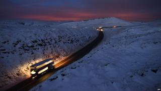 A double-decker bus travels over Standedge between snow-covered fields at dusk near the village of Diggle, northern England, on December 27, 2014.