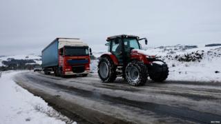 A tractor pulls a lorry up a snow covered hill near Ashbourne