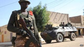 A Malian soldier stands guard as French soldiers patrols next to the central police station, on 11 February 2013 in Gao