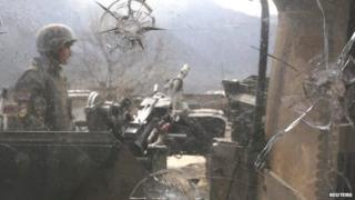 An Afghan National Army (ANA) soldier is seen through damaged glass as he keeps watch at the Forward Base in Nari district near the attacked army outpost in Kunar province