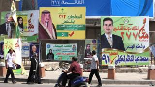 Iraqis walk past election campaign billboards in Kahramana Square, in the capital Baghdad, on 13 April 2014