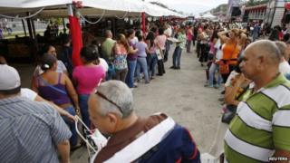 People stand in line to buy food at a state-run street market in Caracas in this 13 November, 2014 file photo.
