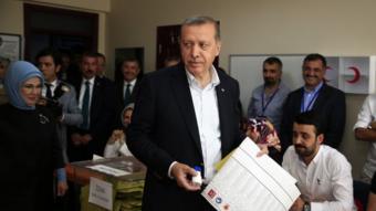 Turkey’s President Recep Tayyip Erdogan, accompanied by his wife Emine, left, holds his ballot as he prepares to vote at a polling station in Istanbul.