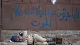 A member of the Syrian civil defence force sleeps on a street in the rebel-held side of city of Aleppo, beside graffiti that says: "Those looking for life under the rubble of death" (8 June 2015)