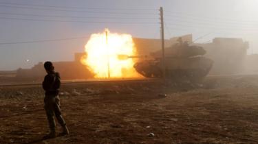 A Syrian rebel fighter stands near a Turkish tank as it fires towards Guzhe village, in the northern Aleppo countryside, (17 October 2016)