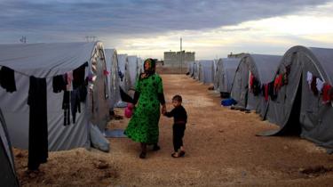 A Syrian Kurdish refugee mother and son from Kobane walk beside their tent in a camp in the south-eastern Turkish town of Suruc, on the Turkish-Syrian border (19 October 2014)