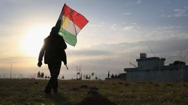 Figura caminando a contraluz con una bandera del Kurdistán iraquí