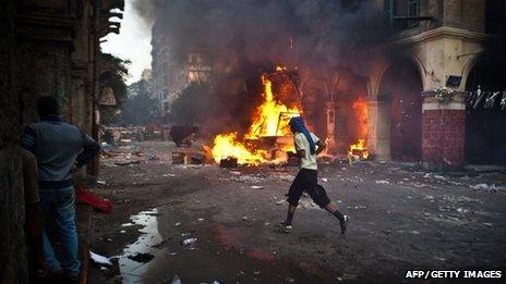 A supporter of the Muslim Brotherhood runs past a burning vehicle in Cairo