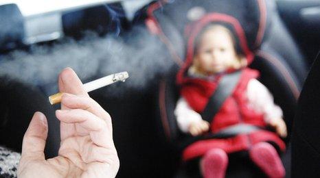 Person smoking in car with a small child in the back seat
