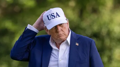 US President Donald Trump wearing a blue suit and a white cap with USA on it
