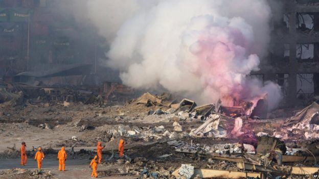 Firefighters in protective gear watch partially pink smoke continue to billow after an explosion at a warehouse in Tianjin (13 August 2015)