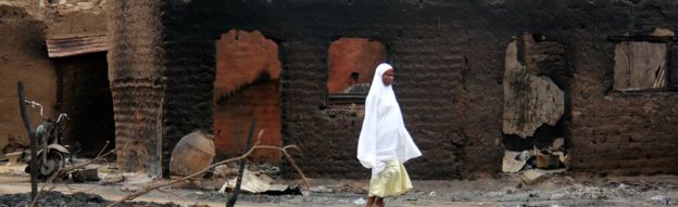 a woman walks past burnt houses in Baga After clashes involving Boko Haram fighers - 2013