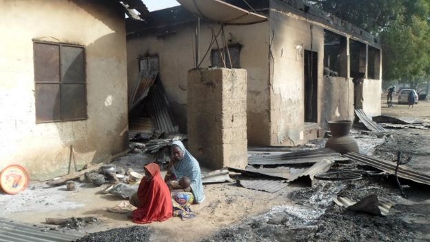 Dos habitantes de Nigeria frente a su vivienda quemada
