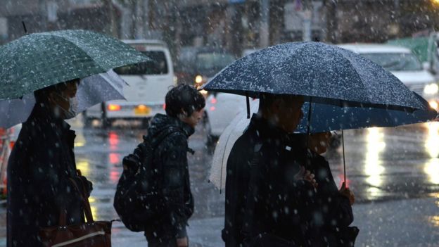 Pedestrians are heading to work in snowfall during the early morning hours in Tokyo on November 24, 2016