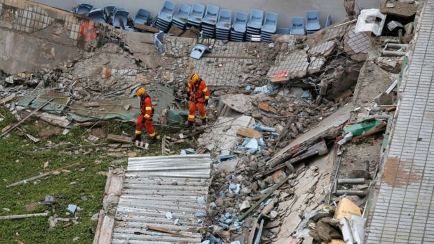 Two firefighters walk through the debris of the collapsed section of a building at the City University