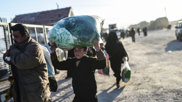 A Syrian boy holds his belongings above his head at a Turkish border crossing