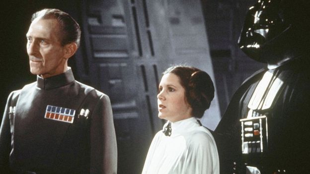 British actors Peter Cushing, David Prowse, and American actress Carrie Fisher on the set of Star Wars: Episode IV - A New Hope in 1977