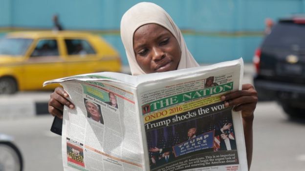A Muslim woman reads a newspapers on a street in Lagos, Nigeria, reporting Trump's victory