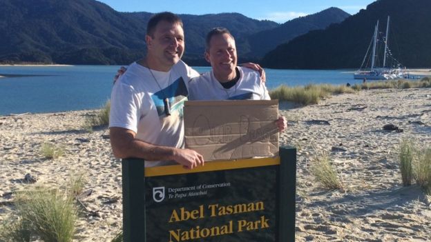 Two campaigners hold a sign saying 'Our beach' as they stand on a beach in New Zealand - 10 July 2016