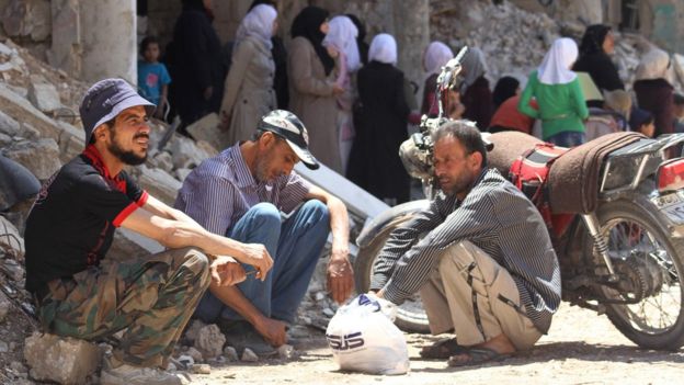 Syrian men sit next to a damaged building in the town of Daraya, southwest of central Damascus, on May 23, 2016