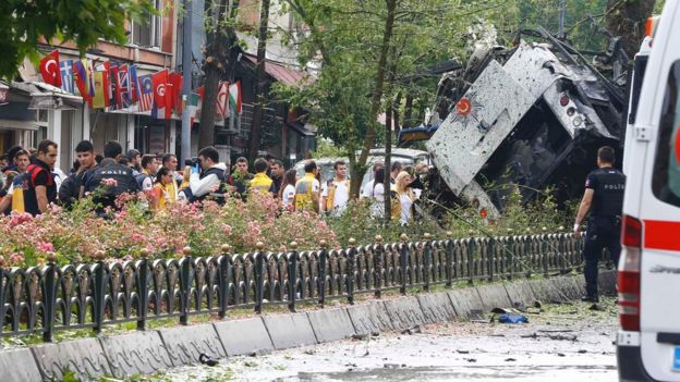 People stand beside beside a Turkish police bus which was targeted in a bomb attack in a central Istanbul