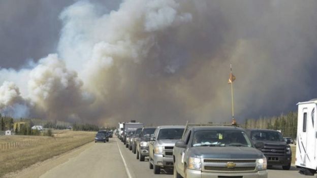 Plumes of smoke rise in the air, as people flee the wildfire in their cars in Fort McMurray