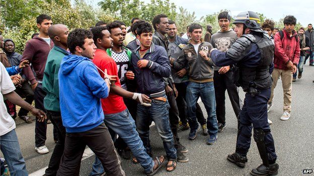 French riot police officer stands as illegal migrants wait to board lorries