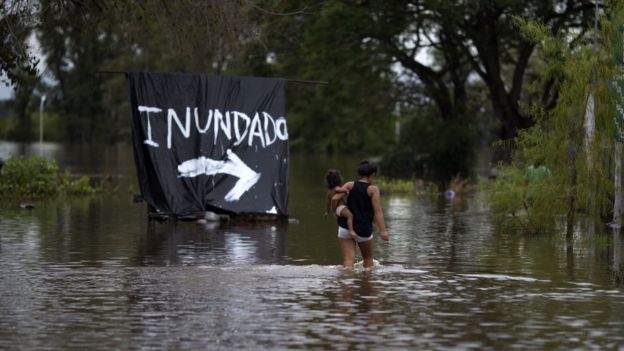 A woman carries her baby through a flooded area of Concordia, Entre Rios province, Argentina