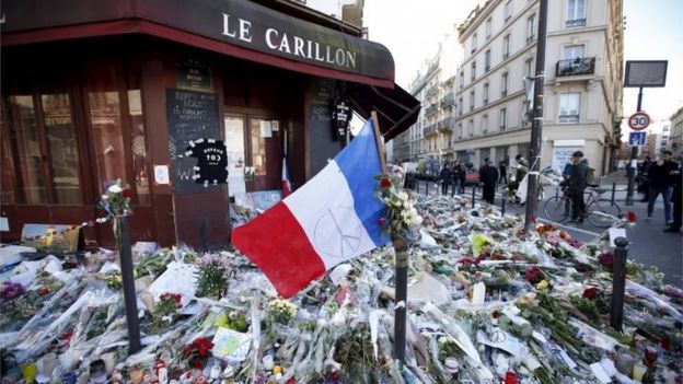 A French flag flies over flowers, candles and messages in tribute to victims outside Le Carillon restaurant, which was attacked on 13 November